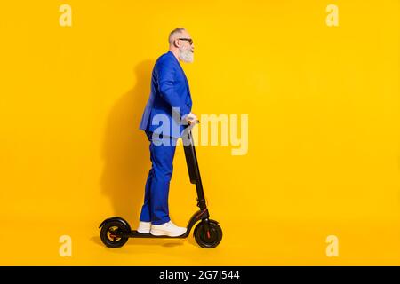 Full size profile side photo of mature businessman riding ecological scooter isolated on yellow color background Stock Photo
