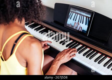 unrecognizable afro american woman learning to play piano with video lessons. Concept of virtual learning. Selective focus on hand Stock Photo
