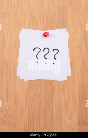 White Sticky Notes with Three Question Marks Pinned to the Wooden Message Board. To Do List Reminder in the Office. Memo Note at Work Stock Photo