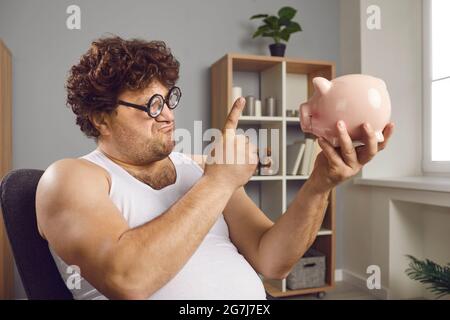 Funny fat man wagging with raised index finger at piggy bank moneybox portrait Stock Photo