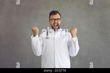 Excited smiling male doctor in medical uniform showing yes hand gesture Stock Photo