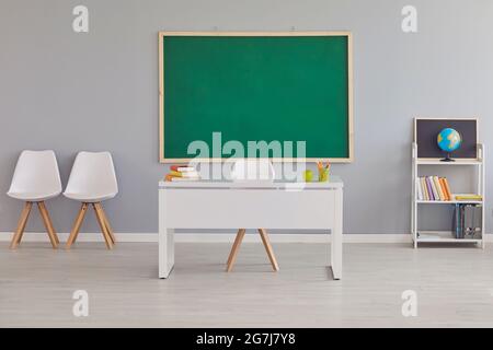 Interior of modern school classroom with teacher's desk and clean green chalkboard Stock Photo