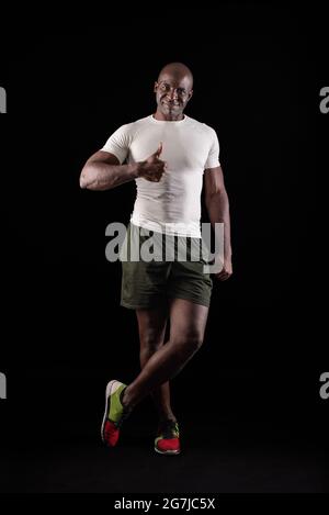 Black man standing looking at camera with thumb up and one leg crossed Stock Photo