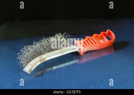 An old wire brush with a red handle on the table. Working tool on a black background Stock Photo