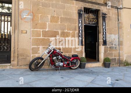PLASENCIA, SPAIN - Mar 23, 2021: A red custom chopper motorcycle parked next to the front of a tattoo shop called The Black Sheep Stock Photo
