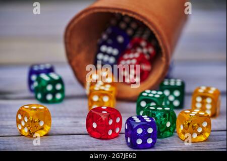 View to different colored game dices and a dice cup on a wooden table. Stock Photo