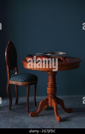Chair, table and violin lying on the table against the background of dark blue walls Stock Photo