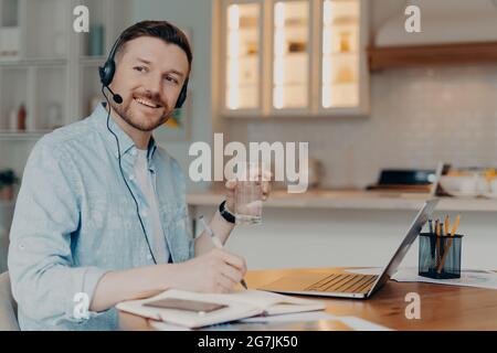 Bearded freelancer making notes in notebook while sitting at his workplace at home Stock Photo