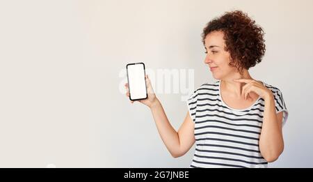 A curly haired Caucasian woman poses next to her mobile phone, looking at camera Stock Photo