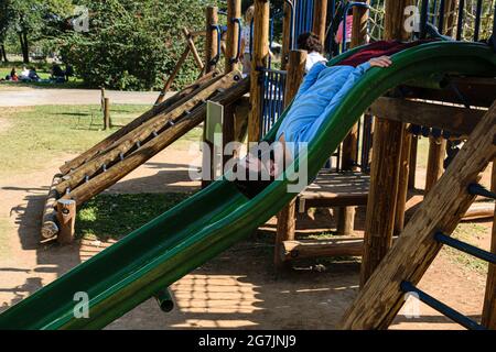 8 year old child in a long-sleeved blue shirt going down a slide upside down. Stock Photo