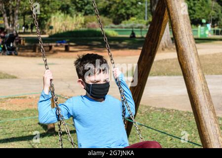 8 year old child, with mask, playing on a swing on a sunny day. Stock Photo