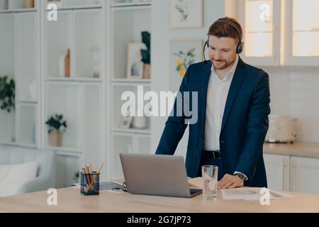 Focused young businessman standing near dining table and working on laptop Stock Photo