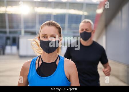 Close up portrait of sportive mature woman wearing black protective mask while running together with her husband in the morning during Covid19 Stock Photo