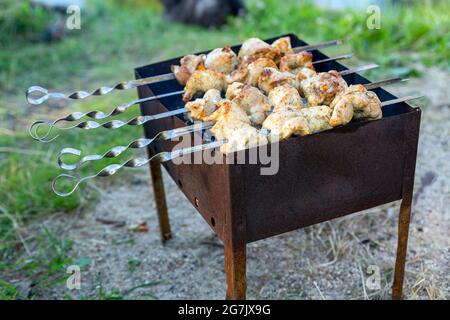 Skewered meat is fried on charcoal close-up on a grill or brazier. Picnic, evening with friends and family, cooking over an open fire in the front or Stock Photo