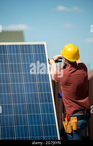 Worker in safety helmet installing photovoltaic panel for customer, view from the back Stock Photo