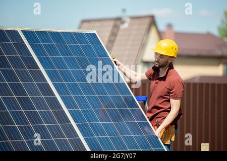 Mounter in hardhat and protective goggles installing solar panel in backyard of house Stock Photo