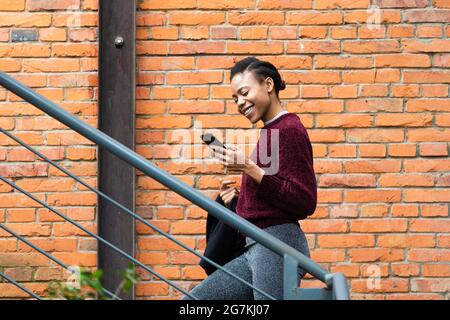 Beautiful beautiful African black female businessman holding a mobile phone walking on the stairs and happily reading messages Stock Photo