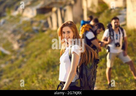 Hiker girl with a big backpack who travels with friends in the mountains. Stock Photo