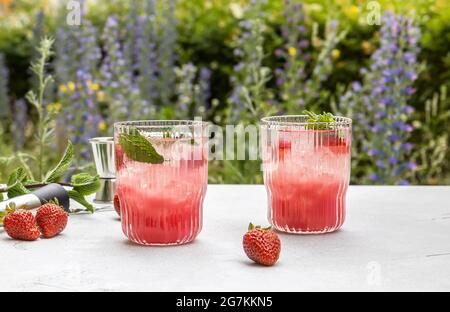 Cold, strawberry mocktail or cocktail with mint, ice cubes in front of the garden. Stock Photo