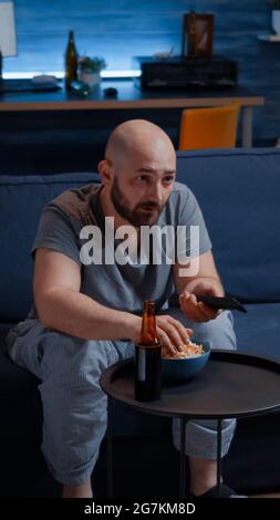 Football sport watching game late at night eating popcorn, cheering beer bottle for favourite winner team. Man enjoying championship entertainment match soccer fan looking at competition on television Stock Photo