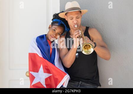 Smiling latina woman leaning on latino man playing the trumpet Stock Photo
