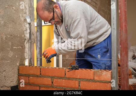 Construction worker taking measurements to build a straight wall. Man bricklaying. Mason laying bricks. Stock Photo