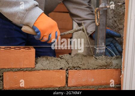 Construction worker putting cement on the brick wall. Man bricklaying. Mason laying bricks. Stock Photo