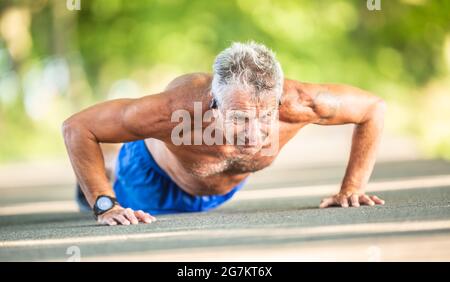 Elderly man doing pushups out on the road in the nature during a sunny summer day. Stock Photo