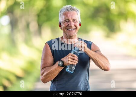 Smiling, fit and retired man with grey hair smiles as he opens up a bottle of water after finishing an aerobic workout. Stock Photo