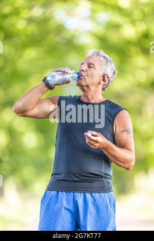 Grey-haired man in his 70s is still fit and drinks water after a workout out in the nature. Stock Photo