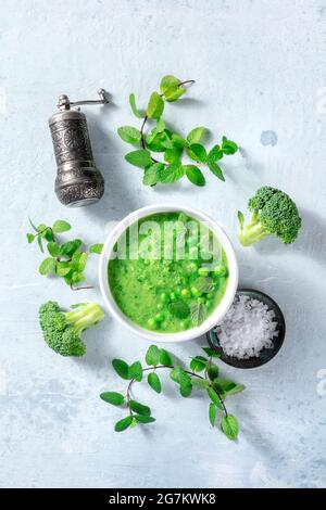 Vegan green soup with ingredients, overhead flat lay shot. Broccoli, green peas, mint, salt, and pepper, healthy organic cuisine, plant-based diet Stock Photo