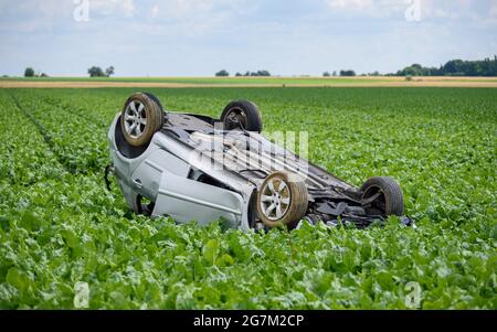 Car turned upside down after accident in a field, a peaceful countryside scenery. Stock Photo
