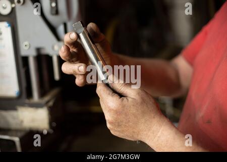 A man pulls out a drill. Installing a drill for a drill. Works in the garage. The master's hands hold the part of the electrical equipment for drillin Stock Photo