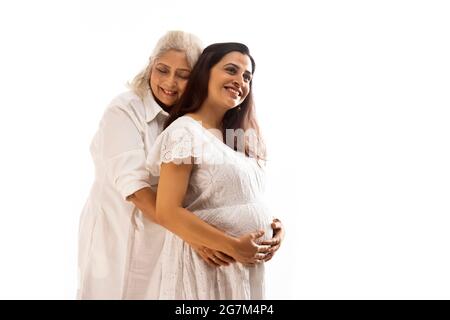 A SENIOR ADULT WOMAN AND PREGNANT DAUGHTER SMILING AND POSING Stock Photo