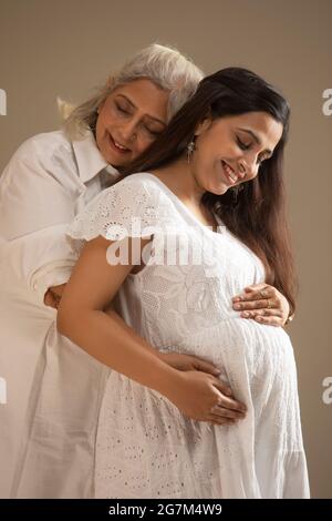 A YOUNG PREGNANT WOMAN AND MOTHER EMBRACING BABY BUMP WITH HAPPINESS Stock Photo