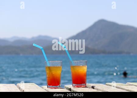 Two glasses with cocktail on a wooden pier on sea and mountains background. Summer vacation on a beach resort Stock Photo