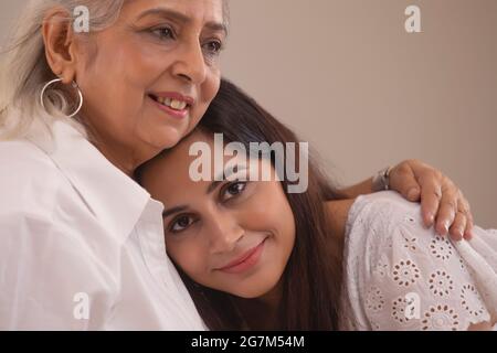 A YOUNG WOMAN LOOKING AT CAMERA WITH A SMILE WHILE MOTHER COMFORTS HER Stock Photo