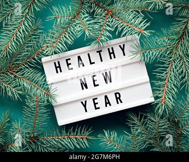 Text Healthy New Year on light board, light box. Greeting flat lay with fir twigs. Simple, minimal end of the year flat lay with greetings text.