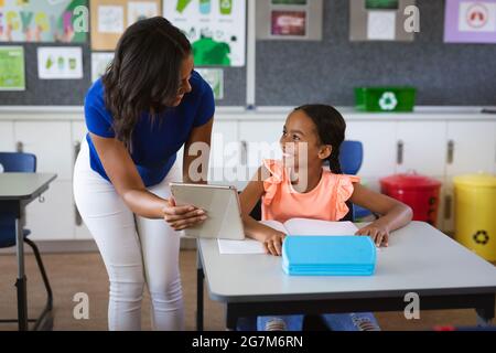 African american female teacher with digital tablet teaching a girl at elementary school Stock Photo