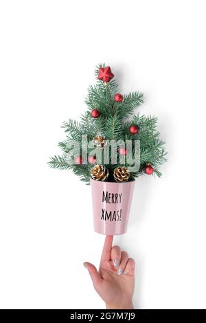 Text Merry Xmas on flower pot with Xmas tree twigs decorated with red Xmas baubles and pine cones. Hand balances it on index finger. Creative Stock Photo