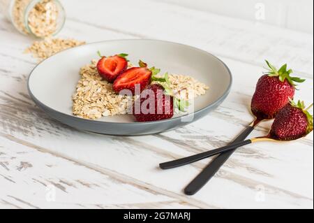 healthy breakfast concept with strawberry and oat flakes in shaoe of heart: strawberry and flakes on a plate closeup Stock Photo