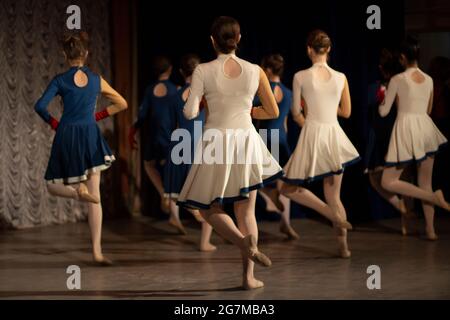 Girls dance on stage. Dance lesson. Beautiful girls in dresses perform. People from the back. Stock Photo