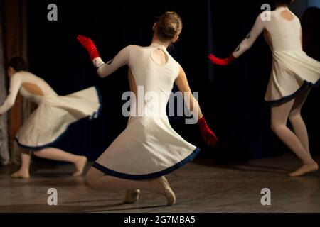 Girls dance on stage. Dance lesson. Beautiful girls in dresses perform. People from the back. Stock Photo