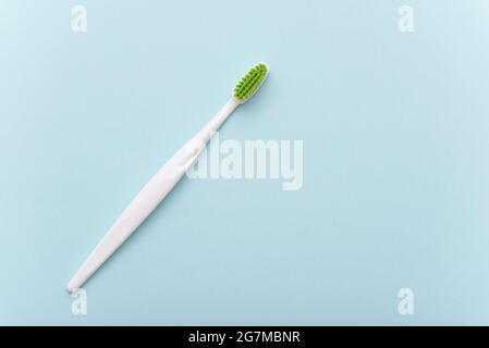 White plastic toothbrush with green bristle as flat lay. Toothbrush on blue surface, top view, space for text. Stock Photo