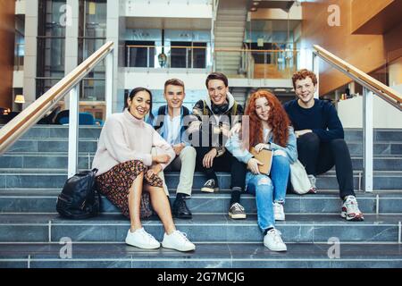 Young students smiling while sitting on college stairs. High school students sitting on steps after class. Stock Photo