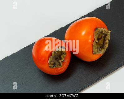 Ripe fresh persimmon fruits on stone cutting board. Stock Photo
