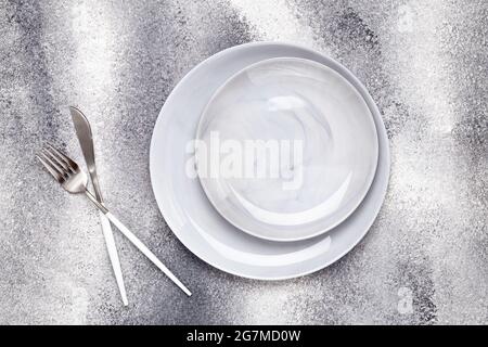 Empty ceramics plate and unused knife with fork, cutlery on gray table, serving concept. Flat lay design. Restaurant menu. Greeting card, layout, mock Stock Photo