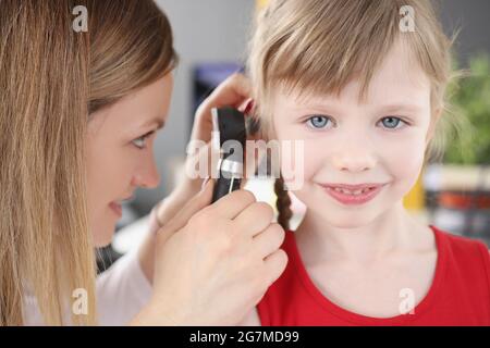 Woman pediatrician looking at eardrum of little girl using otoscope in clinic Stock Photo