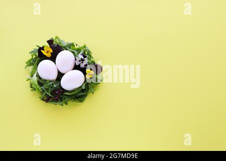 Small egg nest from salad leaves and flowers with white eggs in it. Easter decor Stock Photo