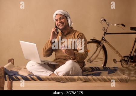 A VILLAGER HAPPILY TALKING ON MOBILE PHONE WHILE DOING ONLINE TRANSACTIONS Stock Photo